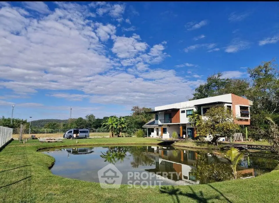 Modern house with pond and lush greenery under a vibrant blue sky, perfect for serene living.