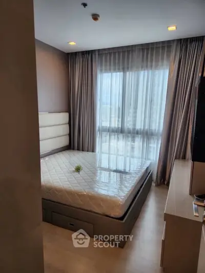 Cozy bedroom with large window and modern furnishings in high-rise apartment.