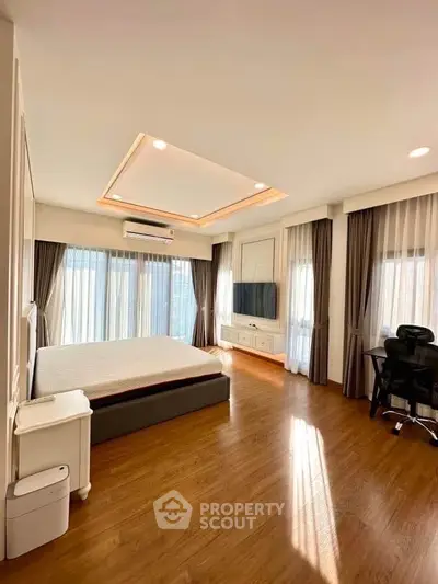 Spacious bedroom with modern decor, large windows, and wooden flooring for a cozy ambiance.