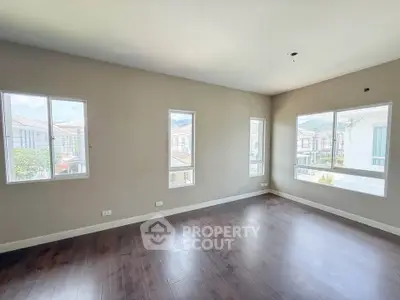 Spacious empty room with large windows and wooden flooring, offering ample natural light and a serene view.