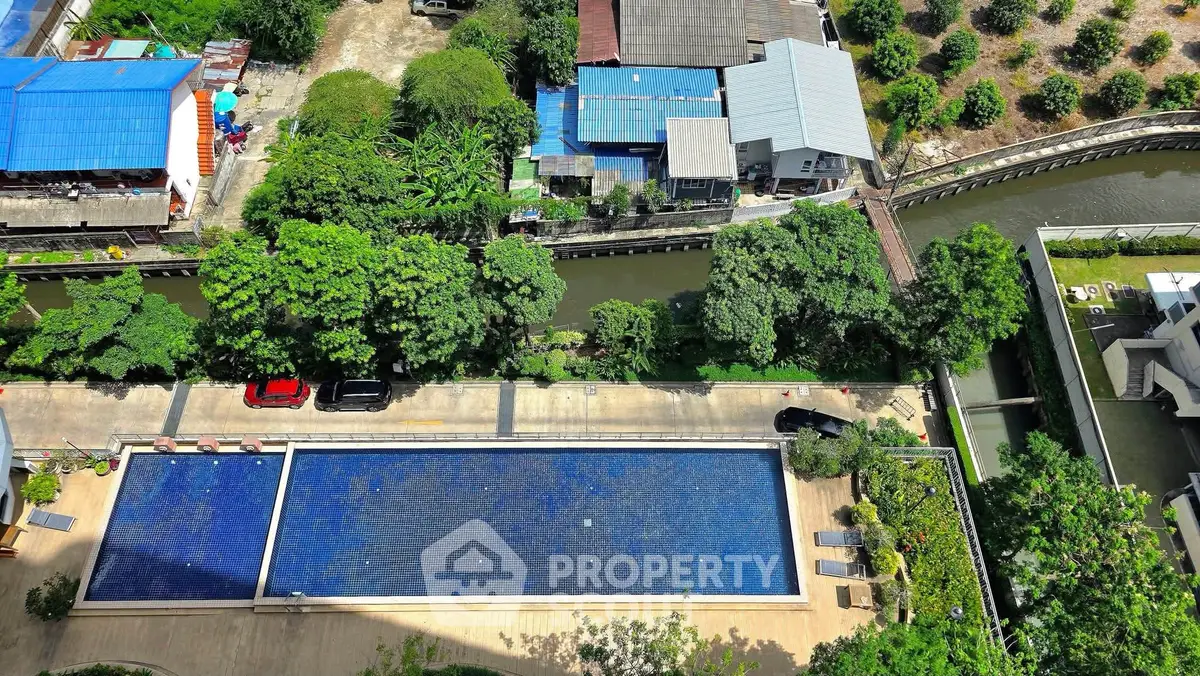 Aerial view of a residential complex with a large swimming pool and lush greenery.