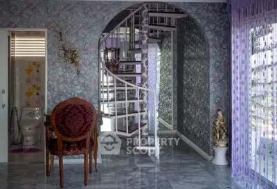 Elegant interior with spiral staircase and floral wallpaper, featuring vintage chair and decorative accents.
