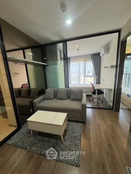 Modern living room with glass partition and cozy workspace, featuring sleek furniture and natural light.