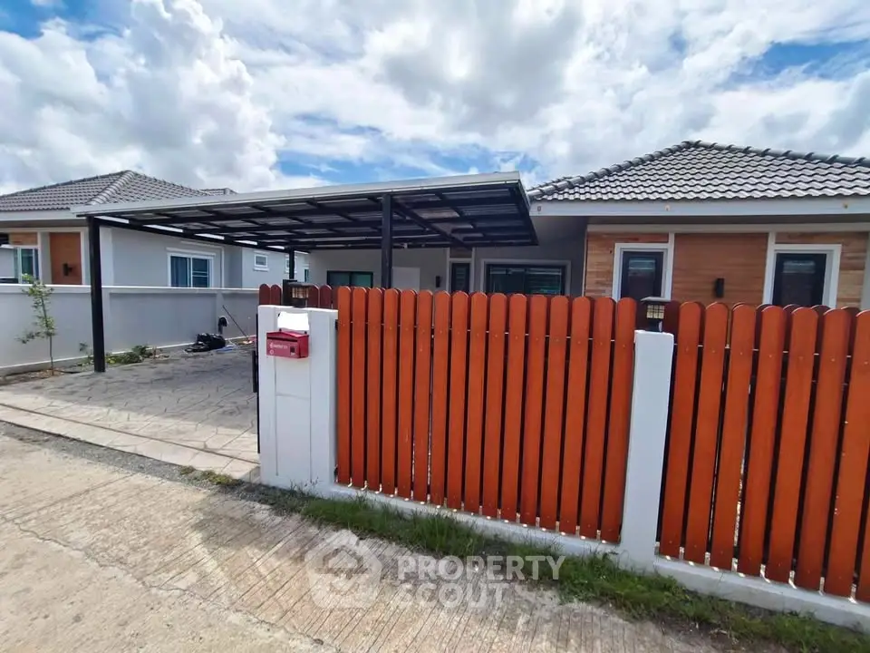 Charming suburban house with modern fence and carport under a cloudy sky.