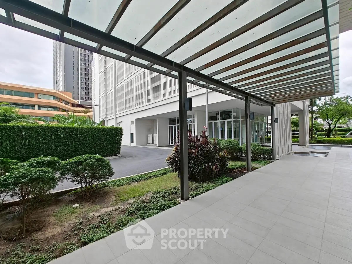 Modern building entrance with sleek glass canopy and landscaped greenery