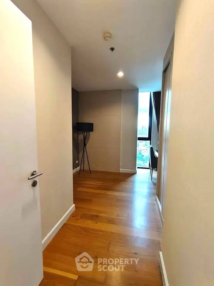 Spacious hallway with wooden flooring leading to a bright room with a view.