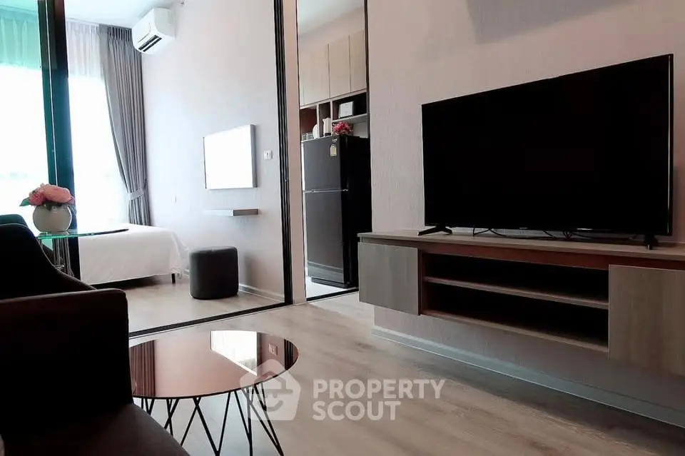 Modern living room with sleek TV unit and view into cozy bedroom, featuring stylish decor and natural light.