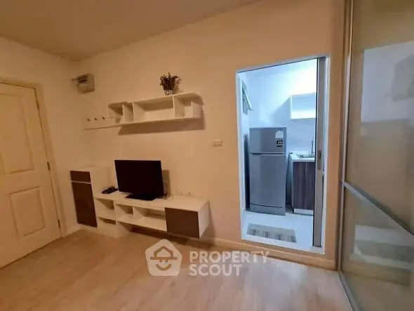 Modern living room with TV and open kitchen featuring sleek appliances.