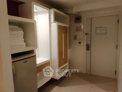 Compact hotel room entrance with mini fridge and storage cabinets