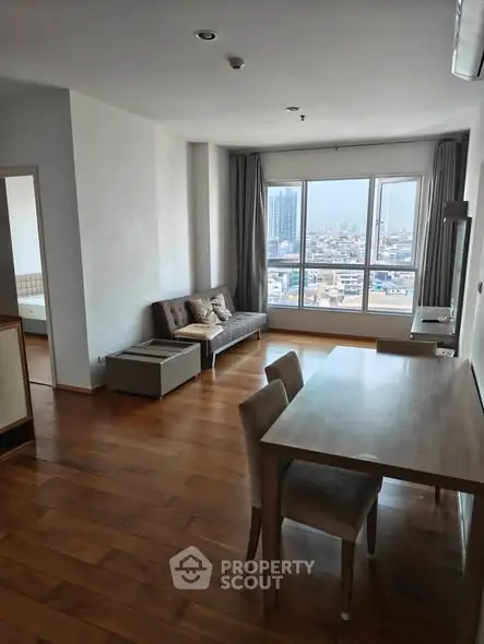 Spacious living room with wooden flooring and city view, featuring modern furniture and large windows.