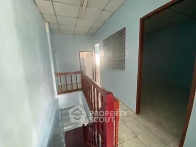 Spacious interior hallway with tiled flooring and wooden railing, ideal for residential or office use.