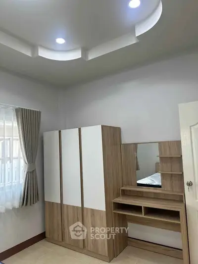 Modern bedroom with stylish wardrobe and vanity set, featuring elegant ceiling design and natural light.