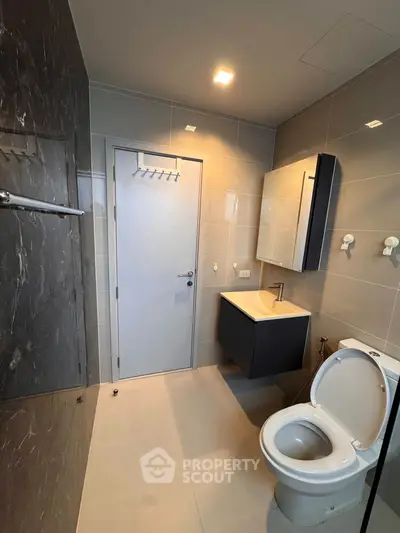 Modern bathroom with sleek fixtures and elegant tile design, featuring a compact vanity and toilet.