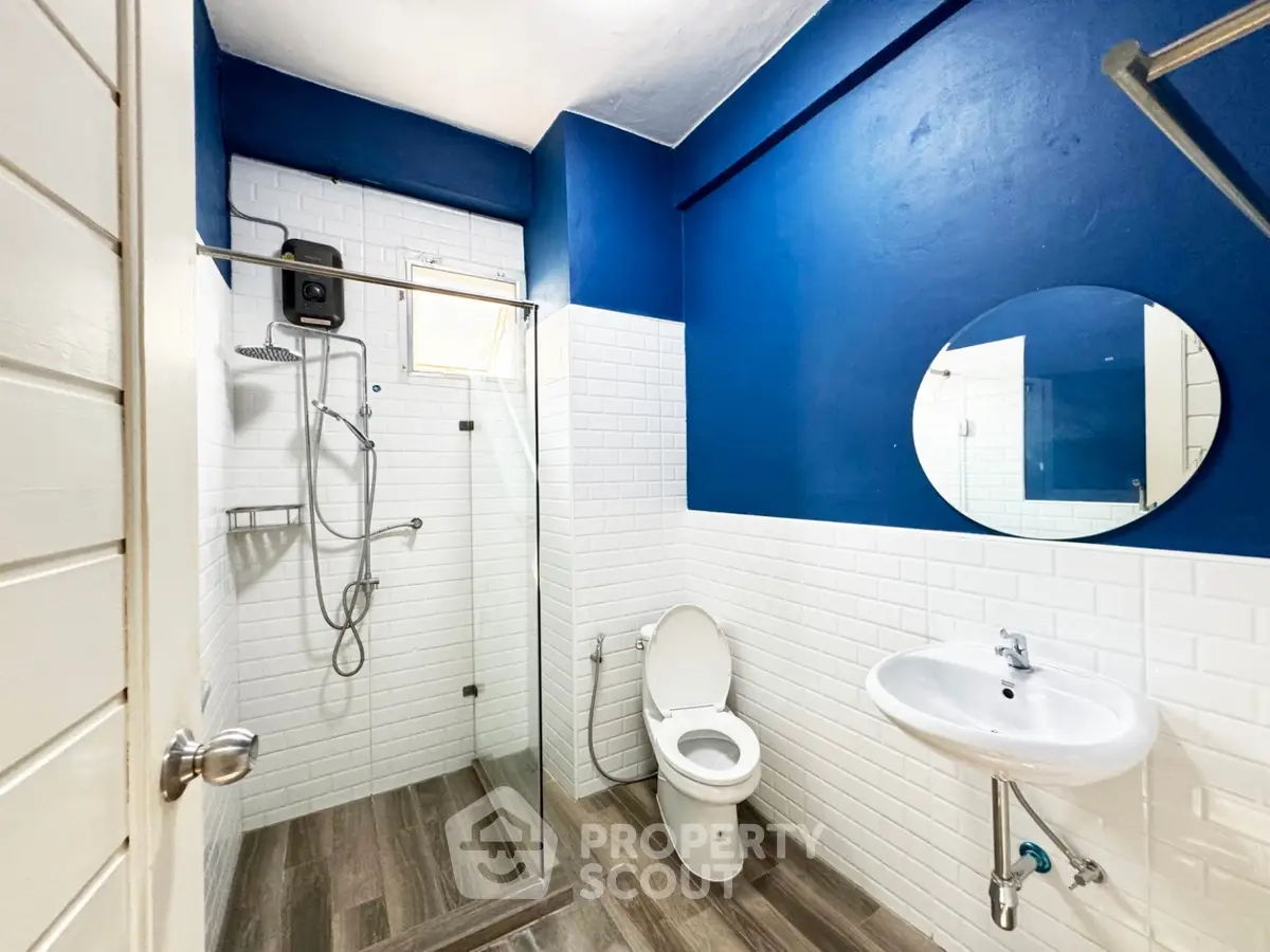 Modern bathroom with blue accent wall and glass shower enclosure.