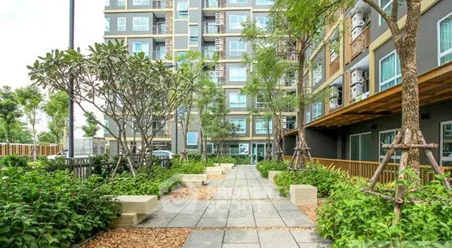 Modern apartment building with lush garden and paved walkway, offering serene urban living.