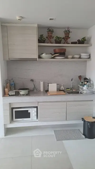 Modern kitchen with sleek cabinetry and open shelving, featuring a microwave and stylish decor.