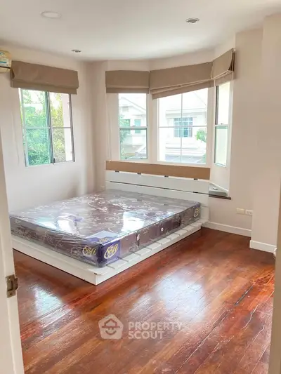 Bright bedroom with large windows and wooden flooring, featuring a new mattress.