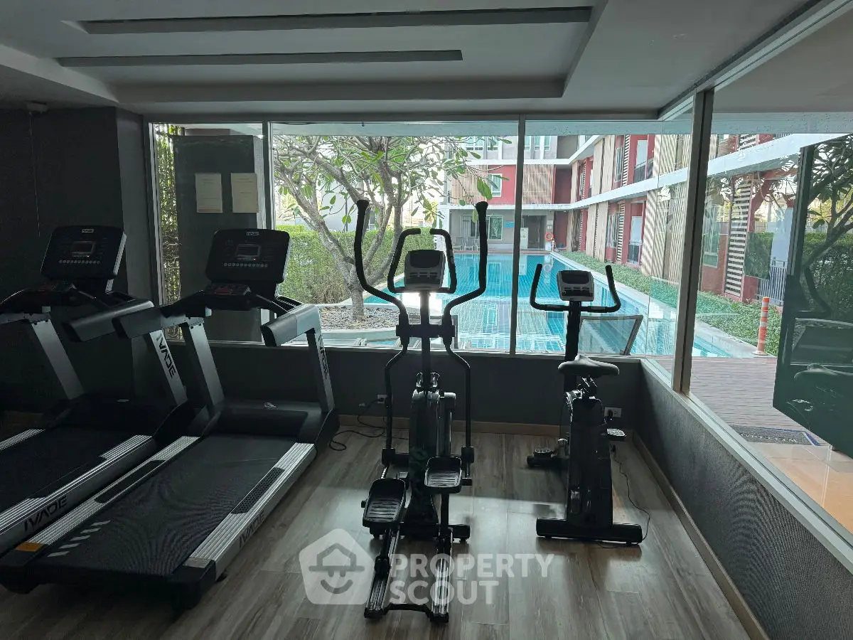 Modern gym with exercise equipment and pool view in luxury apartment complex.