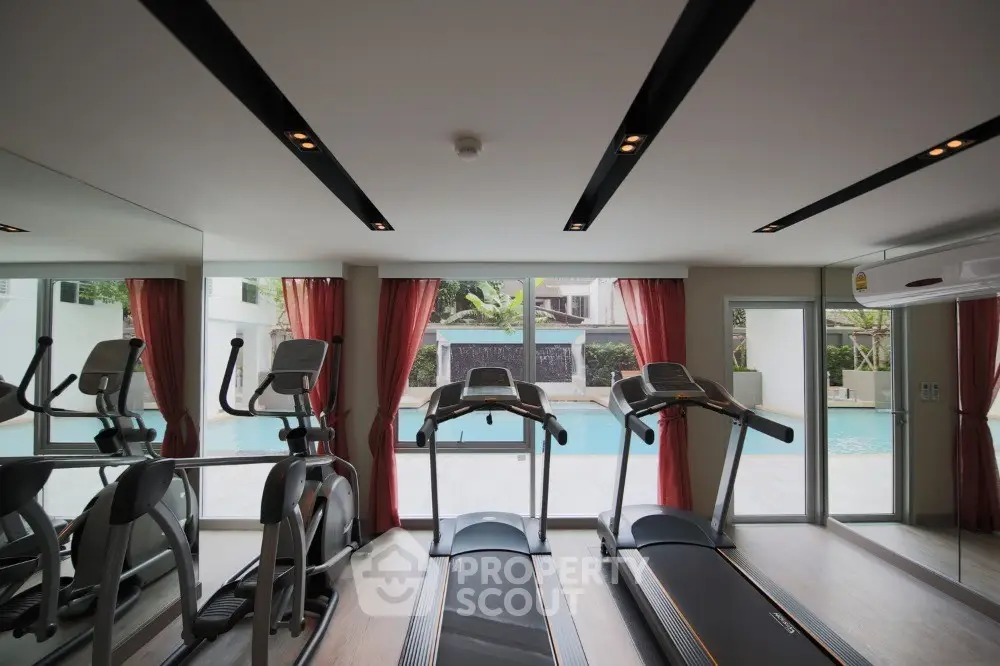 Luxurious gym with pool view, featuring modern treadmills and elliptical machines, ideal for fitness enthusiasts.
