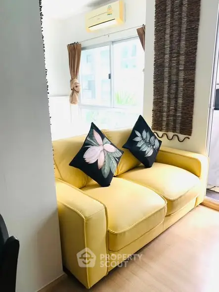 Bright living room with yellow sofa and floral cushions, featuring natural light from large window.