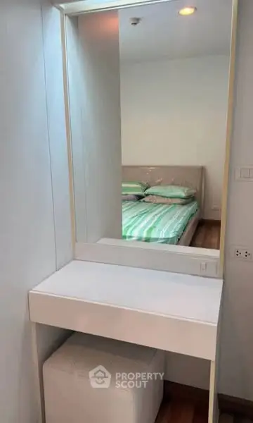 Modern bedroom with stylish vanity and mirror reflecting a cozy bed setup.