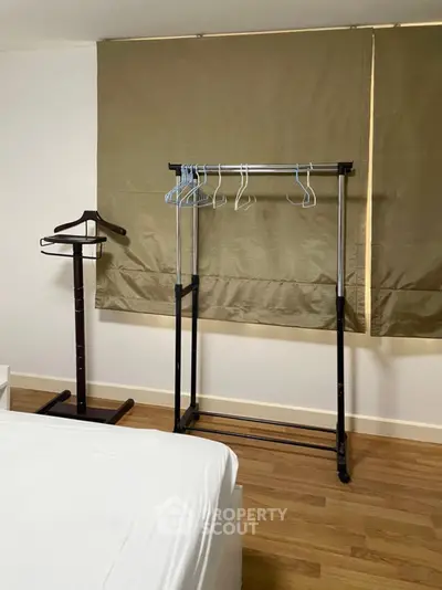 Minimalist bedroom with wooden flooring and clothes rack, ideal for modern living.