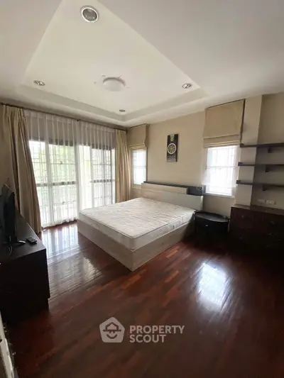 Spacious bedroom with large windows and wooden flooring in modern apartment.