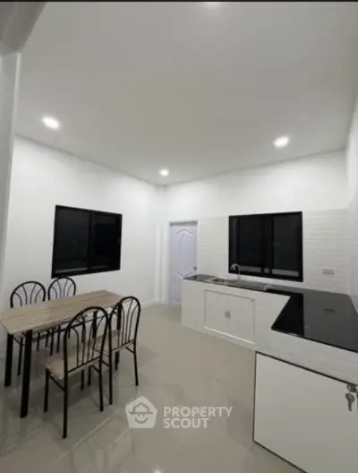 Modern kitchen with sleek design and dining area, featuring minimalist decor and ample lighting.