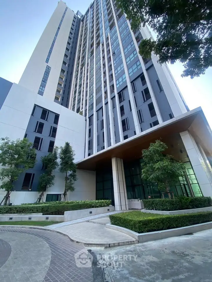 Modern high-rise building exterior with landscaped entrance and tall glass windows.