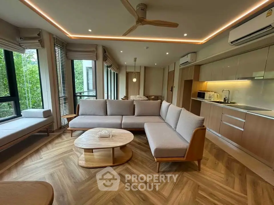 Modern living room with open kitchen, featuring stylish furniture and large windows with natural light.
