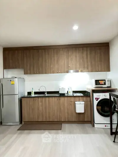 Modern kitchen with wooden cabinets, stainless steel fridge, and washing machine in a sleek apartment.