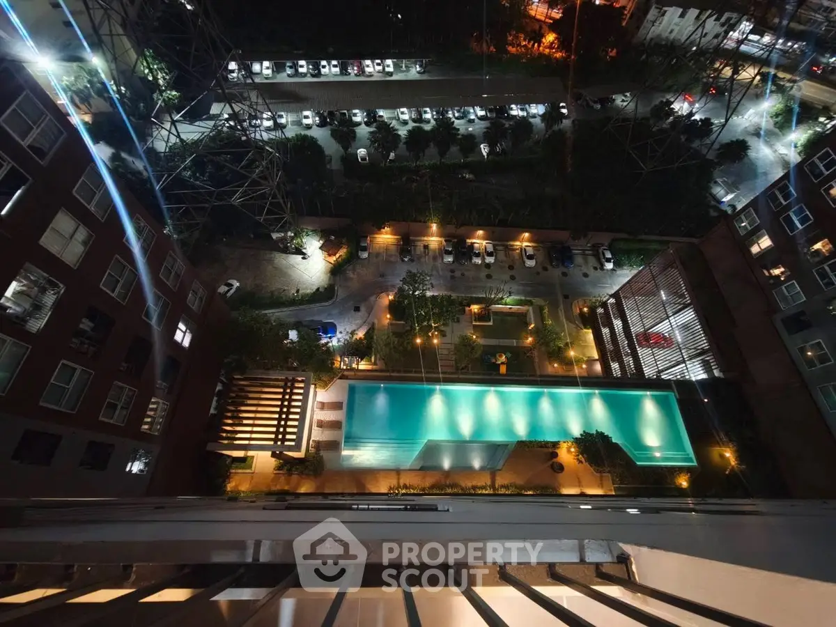 Stunning aerial view of illuminated swimming pool and parking area in modern residential complex at night.
