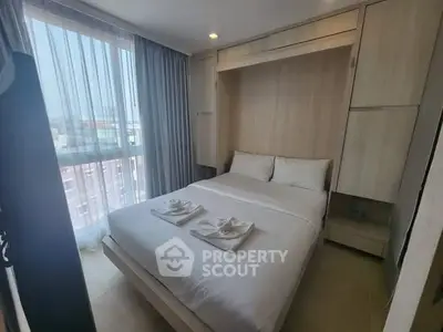 Cozy bedroom with large window and modern furnishings in a high-rise apartment.