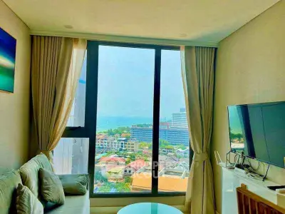 Modern living room with large window offering stunning city and ocean views, featuring cozy seating and a flat-screen TV.