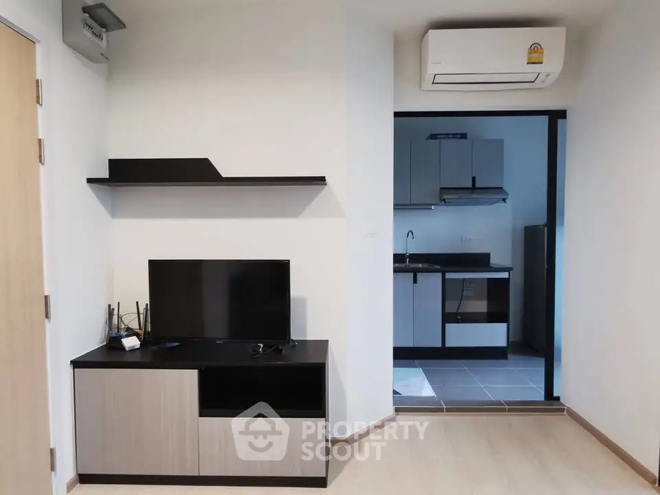 Modern living room with sleek TV stand and view into a compact kitchen area.