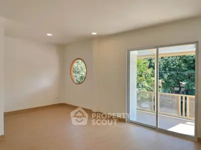 Spacious living room with unique round window and balcony access, perfect for natural light lovers.