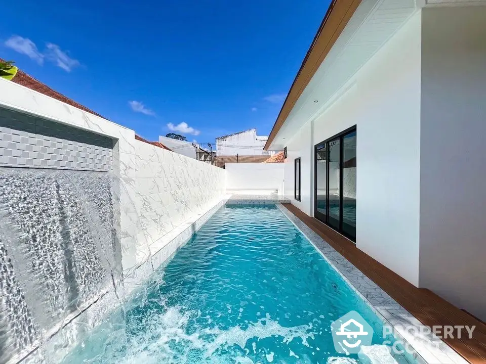 Luxurious modern villa with private pool and waterfall feature under clear blue sky.