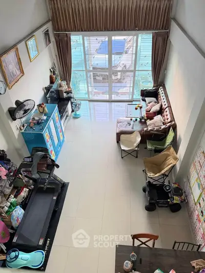 Spacious living room with high ceiling and large windows, featuring cozy seating and modern decor.