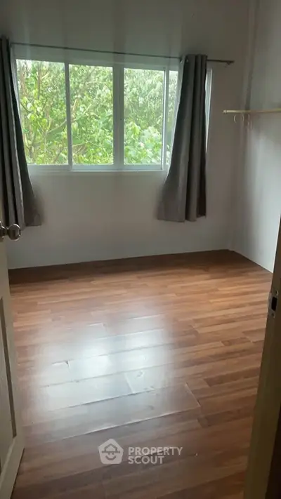 Bright empty room with wooden flooring and large window overlooking greenery