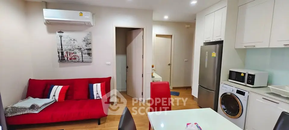 Modern apartment interior with red sofa, kitchen appliances, and wooden flooring.