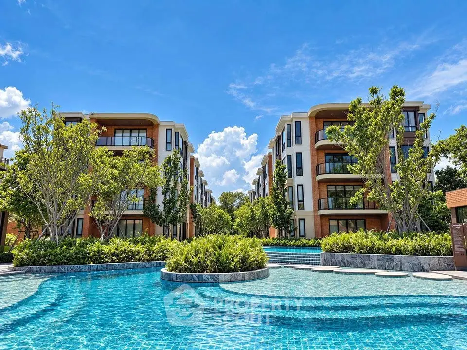 Luxurious apartment complex with stunning pool and lush greenery under a clear blue sky.