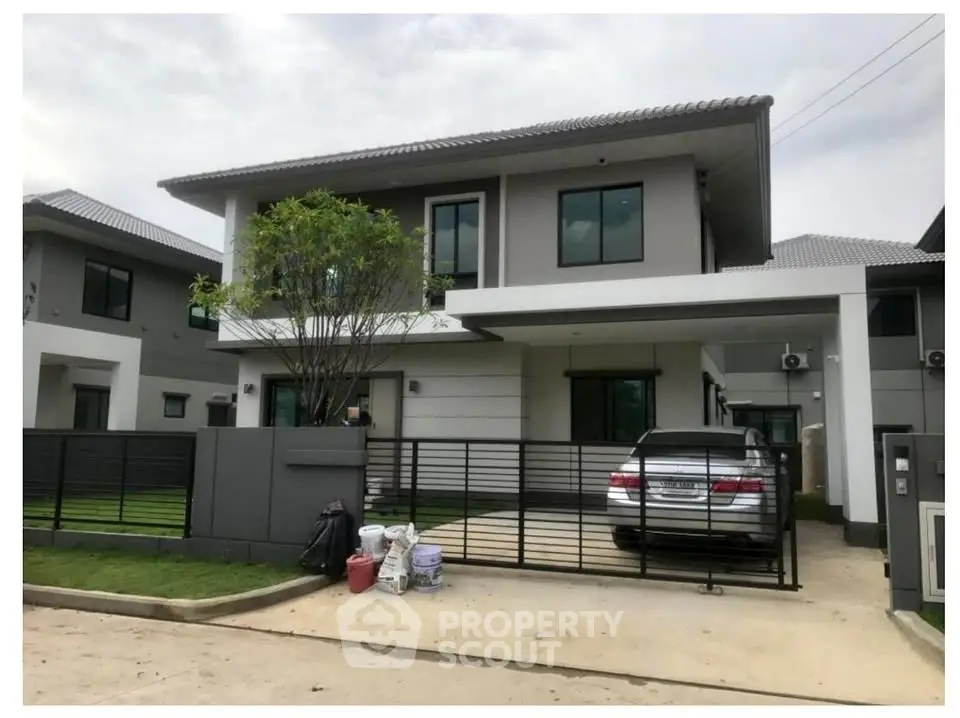 Modern two-story house with driveway and car parked in front, featuring sleek design and lush greenery.