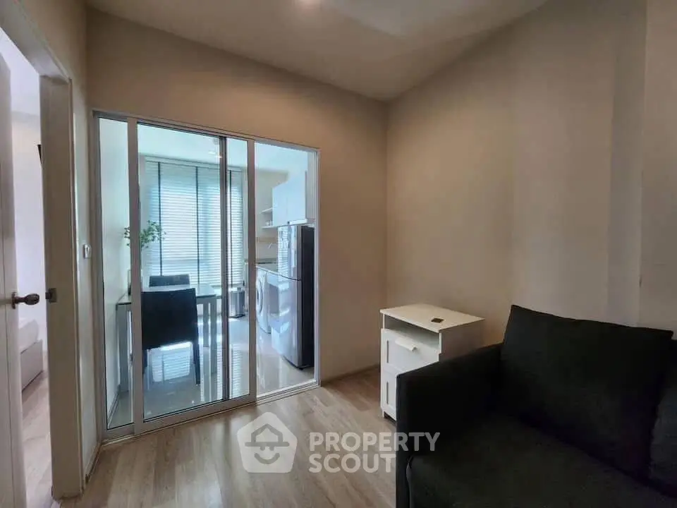 Cozy living room with sliding glass doors leading to a modern kitchen, featuring a sleek black sofa and wooden flooring.