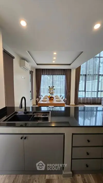 Modern open-plan kitchen with sleek black countertops and elegant dining area with large windows.
