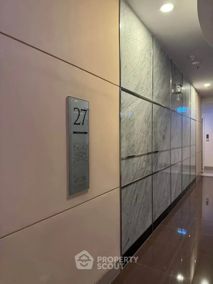 Modern building corridor with sleek marble walls and floor, featuring an elevator panel on the 27th floor.