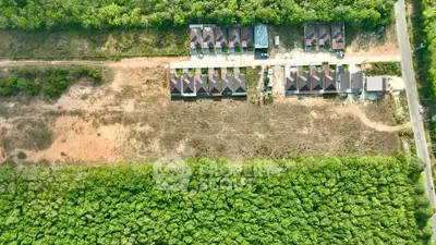 Aerial view of a residential development surrounded by lush greenery and open land.