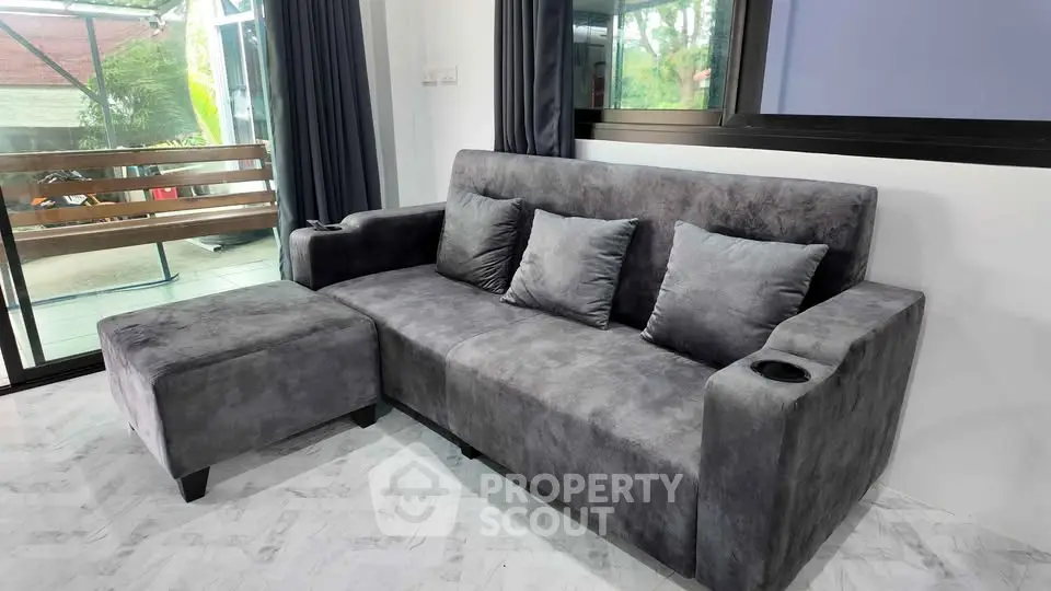 Modern living room with sleek gray sofa and large windows overlooking a lush garden.