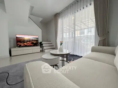 Modern living room with elegant white sofa and large TV, featuring stylish decor and natural light.