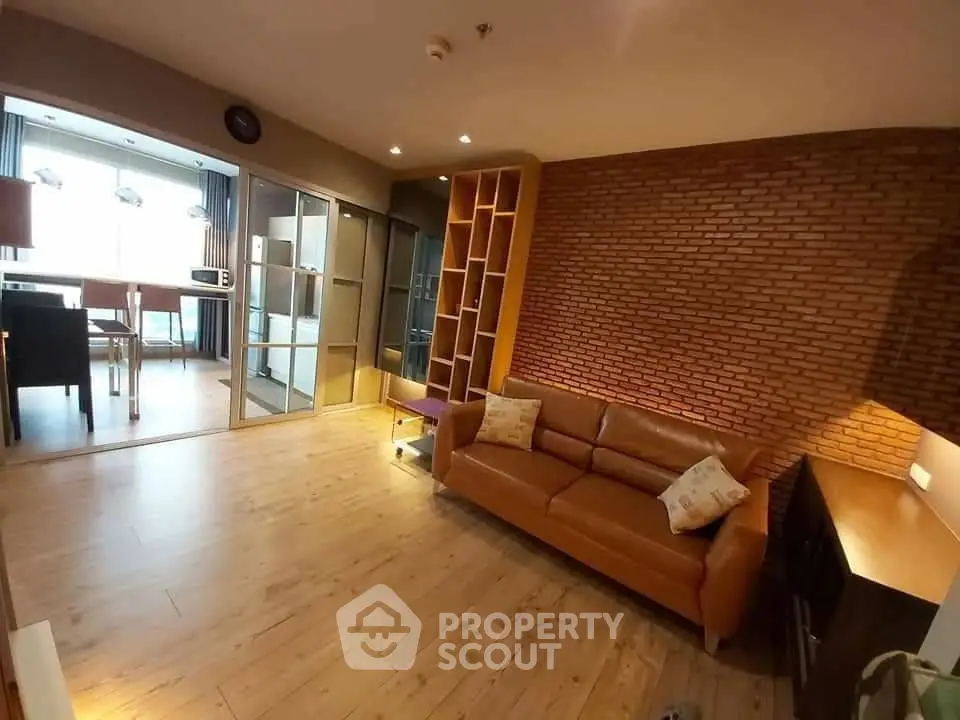 Modern living room with brick accent wall and leather sofa in open layout apartment.