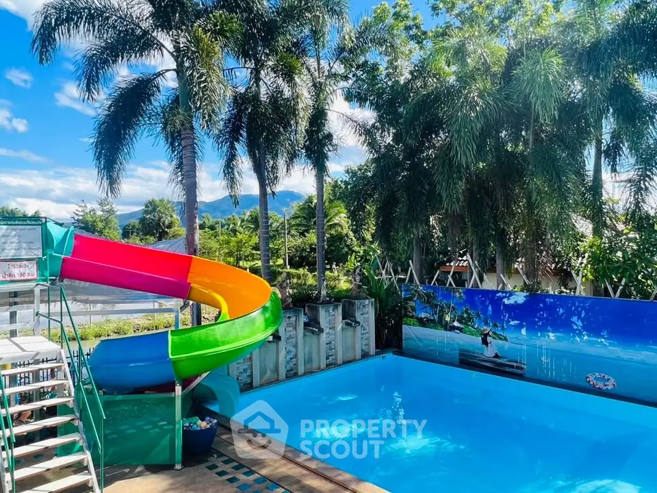 Stunning pool area with vibrant slide and lush palm trees, perfect for relaxation and fun.